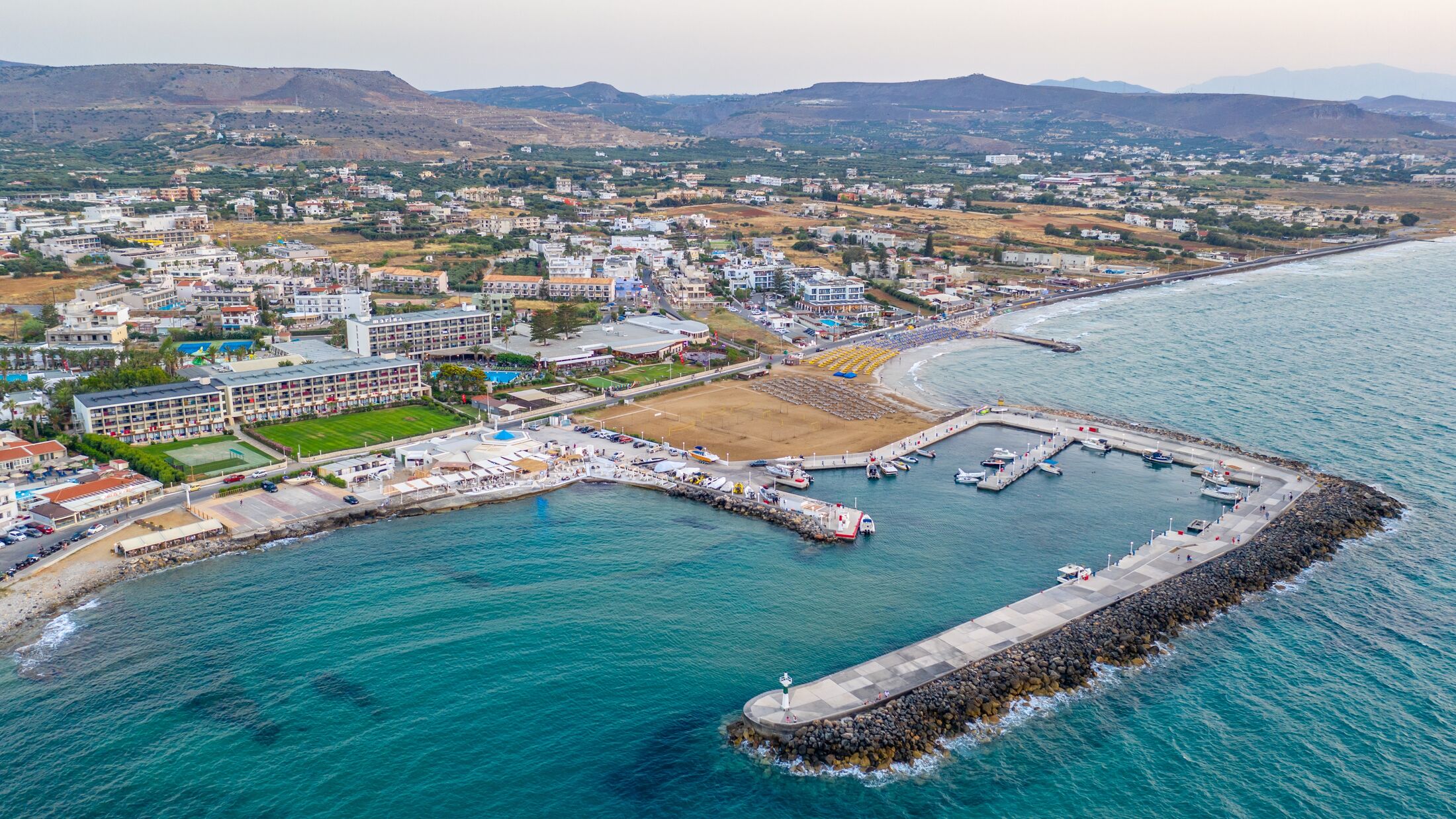 Marina Port Gouves, Crete, Greece - late afternoon drone aerial photo, city landscape, buildings and blue water, sandy beach