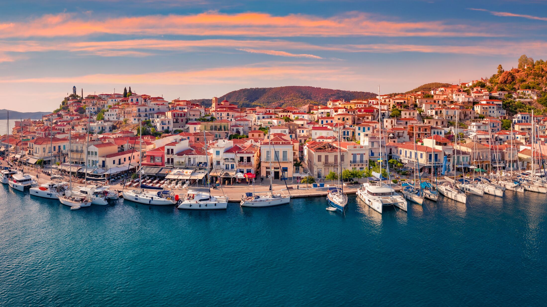 Fantastic sunset in Poros town. Picturesque summer seascape of Myrtoan Sea with a lots of yachts. Attractive evening scene of Peloponnese peninsula, Greece. Traveling concept background.