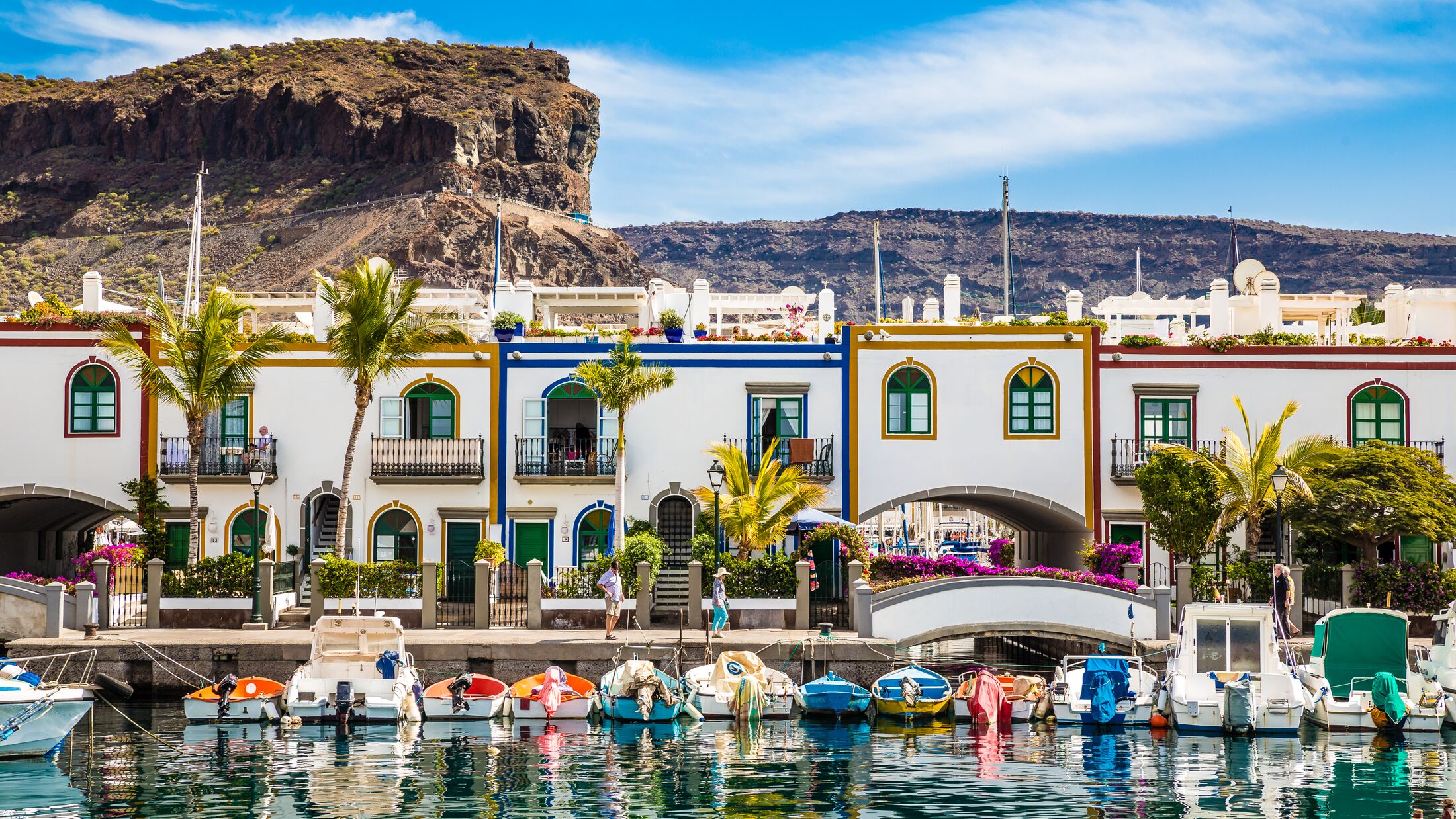 Traditional Colorful Buildings With Boats In Front And Mountain In The Background - Puerto de Mogan, Gran Canaria, Canary Islands, Spain